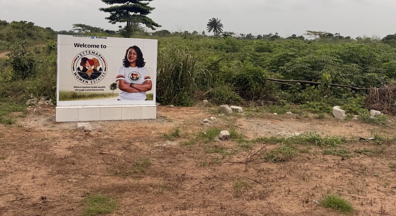 The welcome sign at the entrance to Sytemap Women Estate, Odagwa, with farmland behind it